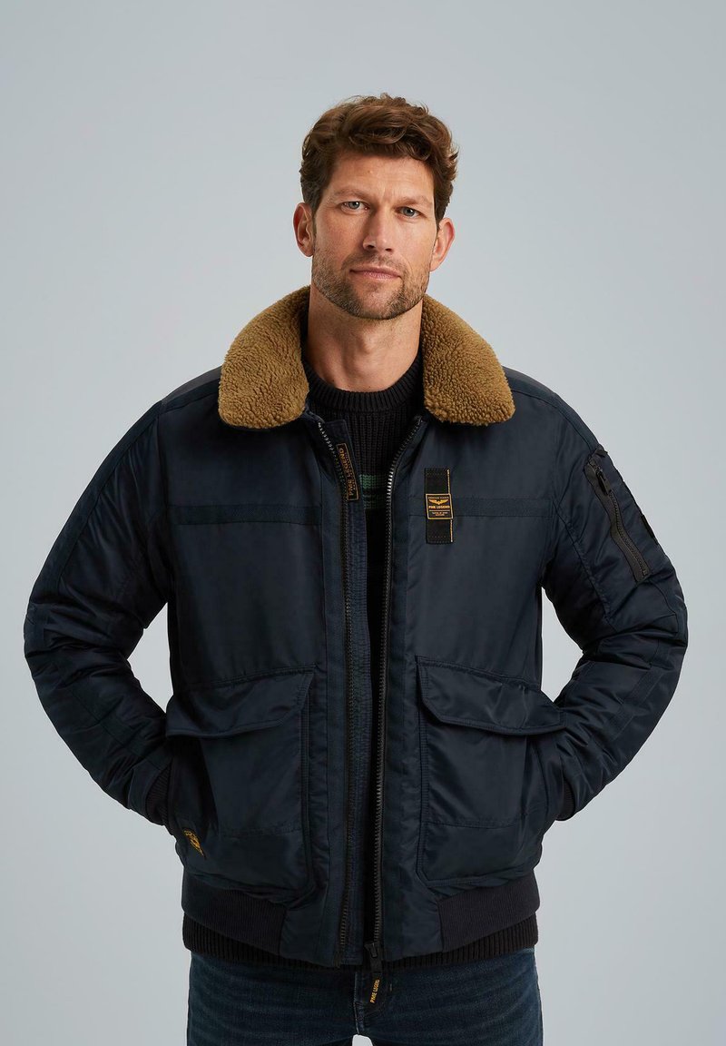 Marineblauer Bomberjacke mit einem braunen, künstlichen Schaffell-Kragen, Frontreißverschluss, mehreren Taschen, gerippten Bündchen und einer weichen, strukturierten Oberfläche.