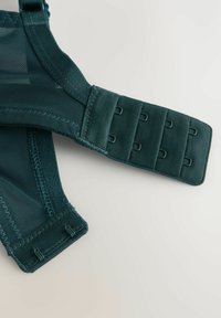 Temno zelena tkanina naramnice modrčka z zapiranjem na kavljčke in zanke, ki vsebuje tri vrste in tri stolpce pritrdilnih kavljčkov.