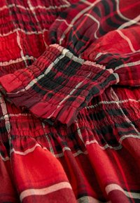 Gros plan d'un tissu à carreaux rouge et noir avec des poignets et une ceinture élastiques froncés, montrant la texture et les détails de la couture.