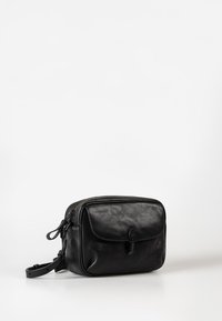 Zwarte leren crossbodytas met voorvak met klep en gespsluiting, verstelbare riem en bovenste ritssluiting op witte achtergrond.