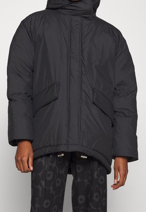 Personne portant une veste matelassée noire avec des poches à rabat sur le devant et un pantalon noir à motifs avec de grandes fleurs.