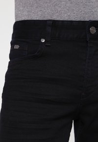 Ciemnoniebieskie dżinsy o ciasnym kroju, z przednimi kieszeniami, z zapięciem na guzik oraz subtelnym przeszyciem wzdłuż szwów.