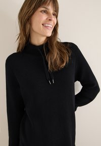 Schwarzer Strickpullover mit hohem Kragen und Kordelzug. Verfügt über eine gerippte Textur und lange Ärmel, mit zwei silberfarbenen Hardware-Akzenten.