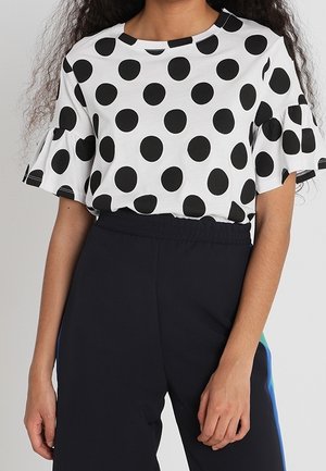 Sort og hvid top med polkaprikker og korte flæseærmer, kombineret med sorte bukser med elastik i taljen. Toppen er lavet af et blødt materiale.