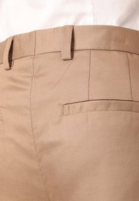 Beige tailored trousers made of woven fabric, featuring a smooth texture, a slim fit, and a single back pocket with subtle stitching detail.