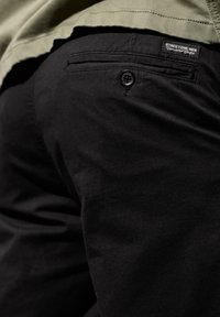 Pantalon en coton noir avec une poche arrière munie d'un bouton et d'une étiquette portant l'inscription "STREETONE MEN". Le tissu présente une texture lisse.