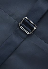 Marineblauer Stoff mit strukturiertem Finish, ausgestattet mit einer Metall-Schnalle und -Riemen, genähten Kanten und einem eleganten, minimalistischen Design.