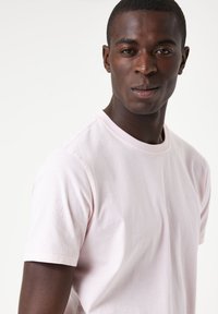 T-shirt en coton rose clair avec des manches courtes, un col rond, et un logo discret sur la poitrine. Texture lisse, design ajusté.