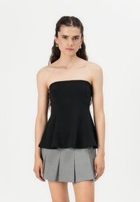 Top nero senza spalline con corsetto aderente e orlo peplum. Abbinato a una mini gonna grigia plissettata. Texture liscia, senza motivi visibili.