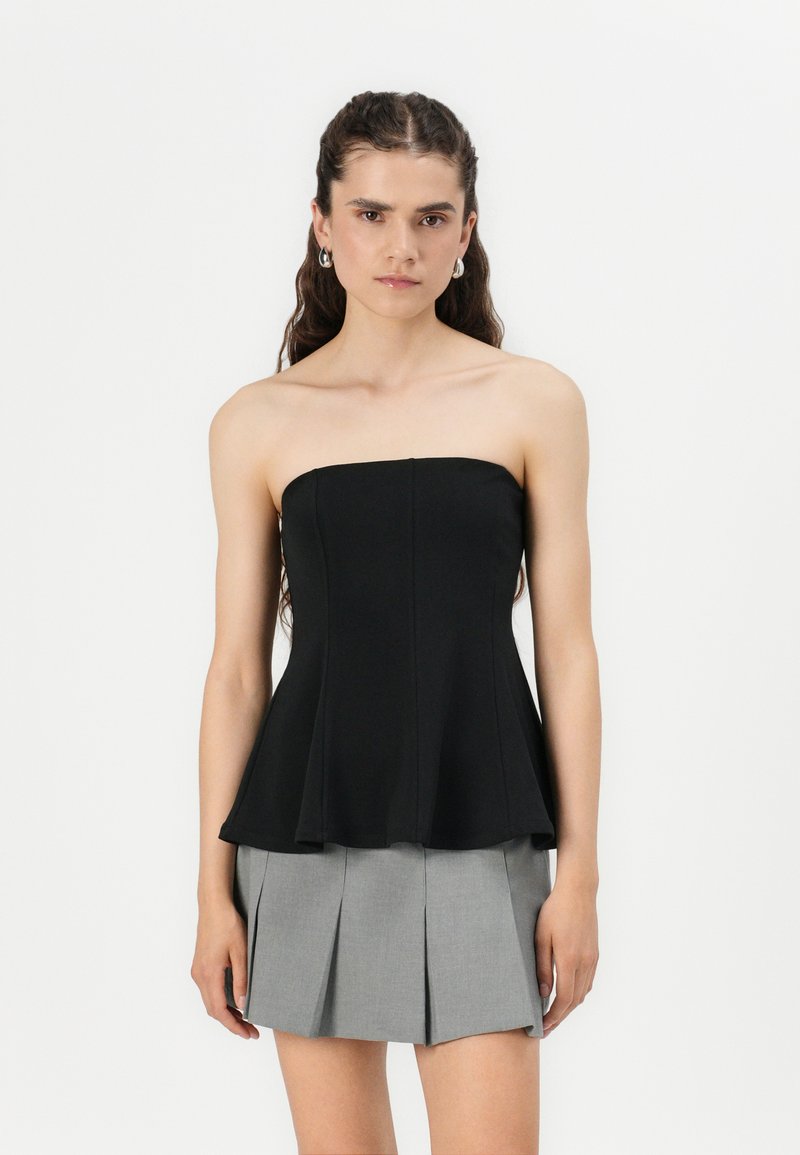 Haut noir sans bretelles avec un corsage ajusté et un ourlet en peplum. Associé à une minijupe plissée grise. Texture lisse, sans motifs visibles.