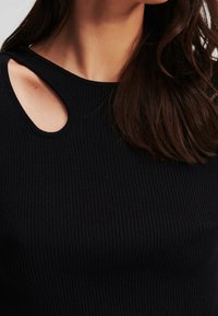 Svart ribbad stickad topp med cirkulär axelsnitt, med rund halsringning och en strukturerad yta.