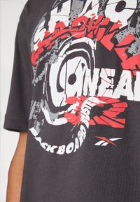 Mørkegrå bomulds T-shirt med kraftig rød og hvid grafisk tekst samt cirkulære designelementer. Korte ærmer med en afslappet pasform.