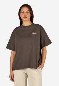 Tmavo hnedé, nadmerné tričko s okrúhlym výstrihom a krátkymi rukávmi. Na hrudi je malé biele logo "Pegador".