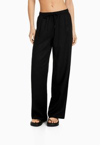 Svarta vida byxor med elastisk midja och dragsko. Tillverkade av ett lätt tyg, med en slät textur och minimalistisk design.