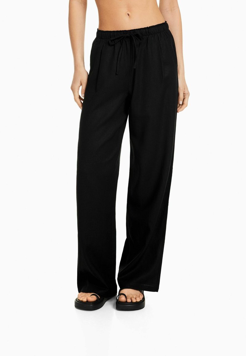 Svarta vida byxor med elastisk midja och dragsko. Tillverkade av ett lätt tyg, med en slät textur och minimalistisk design.