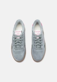 Tenisi gri din suede cu accente roz, având șireturi, zonă perforată pe vârf și talpă din cauciuc maro. Logo-ul este afișat pe limbă.