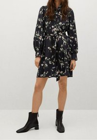 Vestito scuro a stampa floreale con colletto, maniche lunghe a sbuffo e vita legata. Abbinato a stivaletti neri alla caviglia con punta quadrata.