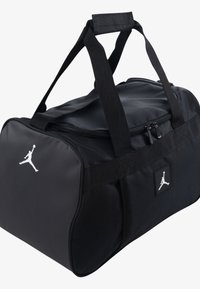 Black duffel bag with zip closure, fabric material, two fabric handles, and white Jumpman logo on side. Square logo patch also visible.