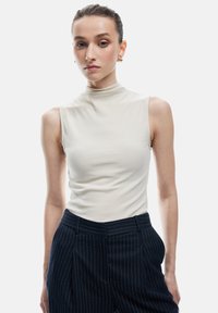 Top sin mangas de color beige claro con textura suave, combinado con pantalones de raya diplomática en navy que presentan un corte a medida y bolsillos frontales.