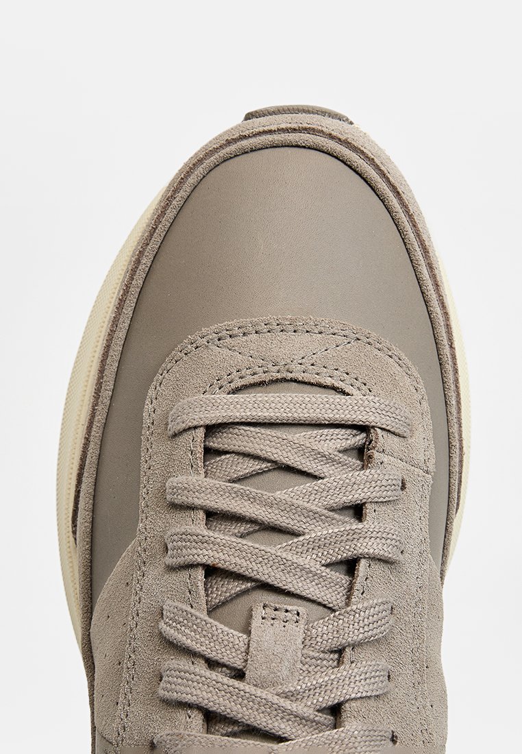 Sneaker grigio caratterizzato da una combinazione di pelle liscia e suede texturizzato. Sistema di allacciatura chiusa con lacci piatti e suola beige.