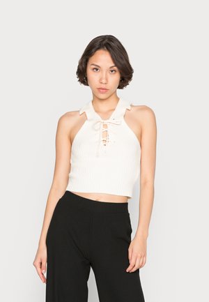 Top curto branco com nervuras, gola e detalhe frontal com cordão, combinado com calças largas pretas com nervuras. Textura suave, design ajustado.