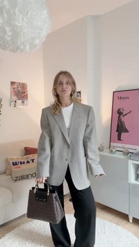 Gray checked oversized blazer over a white top, paired with black wide-leg pants. The model holds a brown patterned handbag.