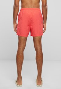 Coral swim shorts with an elastic waistband, above-the-knee length, and a textured fabric finish. No additional pockets or patterns visible.