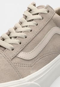 Beige semsket skinn-sneaker med en teksturert overflate, med kremfargede snørebånd og en hvit gummisåle. Diskret merking på siden.