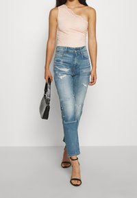 Světlý růžový krajkový body s designem jednoho ramene, v kombinaci se světlými modrými roztrhanými džínami s vysokým pasem a černými sandály na vyšším podpatku.