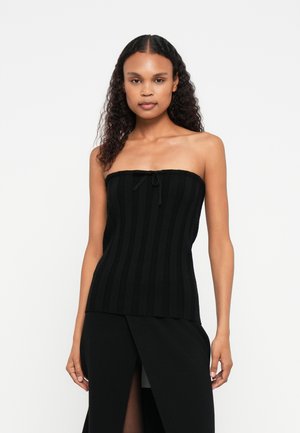 Top preto sem alças com textura canelada vertical e um detalhe de laço no centro. O tecido parece suave e ajustado ao corpo.