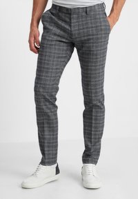 Grijze geblokte broek van lichtgewicht stof, met een getailleerde pasvorm, riemlussen en een knoopsluiting, gecombineerd met witte sneakers.