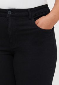 Jean en denim noir au design ajusté, avec une poche avant, des passants de ceinture et une fermeture à bouton à la taille.