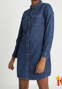 Ballonim denim-kjole med lange ærmer, knaplukning foran, to brystlommer og en lys blå nuance. Har en klassisk krave og let struktur.