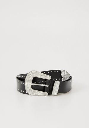 Une ceinture en cuir noir avec des clous en argent, dotée d'une grande boucle ornée de strass, d'un embout et d'une boucle, enroulée sur un fond blanc.