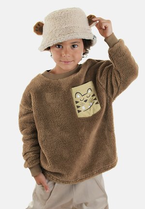 Brauner Fleece-Pullover mit einer hellbeigen Tasche, die ein Tigermotiv zeigt; kombiniert mit einem beigen Bucket Hat mit Bärenohren.