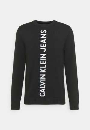 Suéter negro de manga larga tejido, con puños y cuello acanalados, que presenta texto blanco vertical "CALVIN KLEIN JEANS" en el centro frontal.