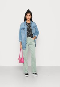 Jaqueta de denim, top preto com flores, calças de veludo cotelê verde menta, bolsa rosa, ténis preto e branco. Texturas suaves, corte descontraído, cores vibrantes.