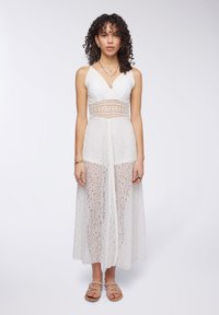 Abito maxi bianco in pizzo con scollatura a V, spalline sottili regolabili e parte inferiore trasparente caratterizzata da un motivo floreale e uno spacco frontale.