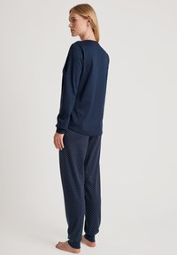 Marineblauw lange mouwen pyjamashirt met ronde hals, gecombineerd met pyjamabroek met stippen. Zacht materiaal, relaxte pasvorm, ribgebreide manchetten aan de broek.