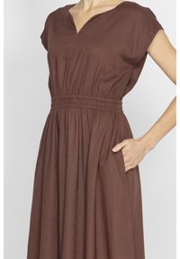Brąsowy sukienka na ramiączkach z dekoltem w kształcie litery V, marszczonym w pasie i bocznymi kieszeniami. Wykonana z tkaniny o fakturze, z lejącą się spódnicą sięgającą do kolan.