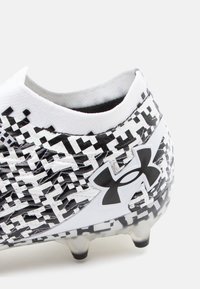 Scarpa da calcio in bianco e nero con un motivo testurizzato, materiale sintetico, design a taglio basso e logo Under Armour in evidenza sul lato.