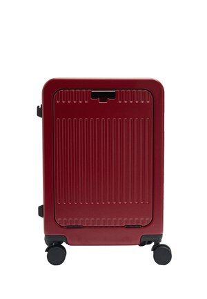 Czerwona walizka z twardą skorupą z pionowymi żebrowaniami, czarnym zatrzaskiem i czterema czarnymi obrotowymi kółkami na białym tle.