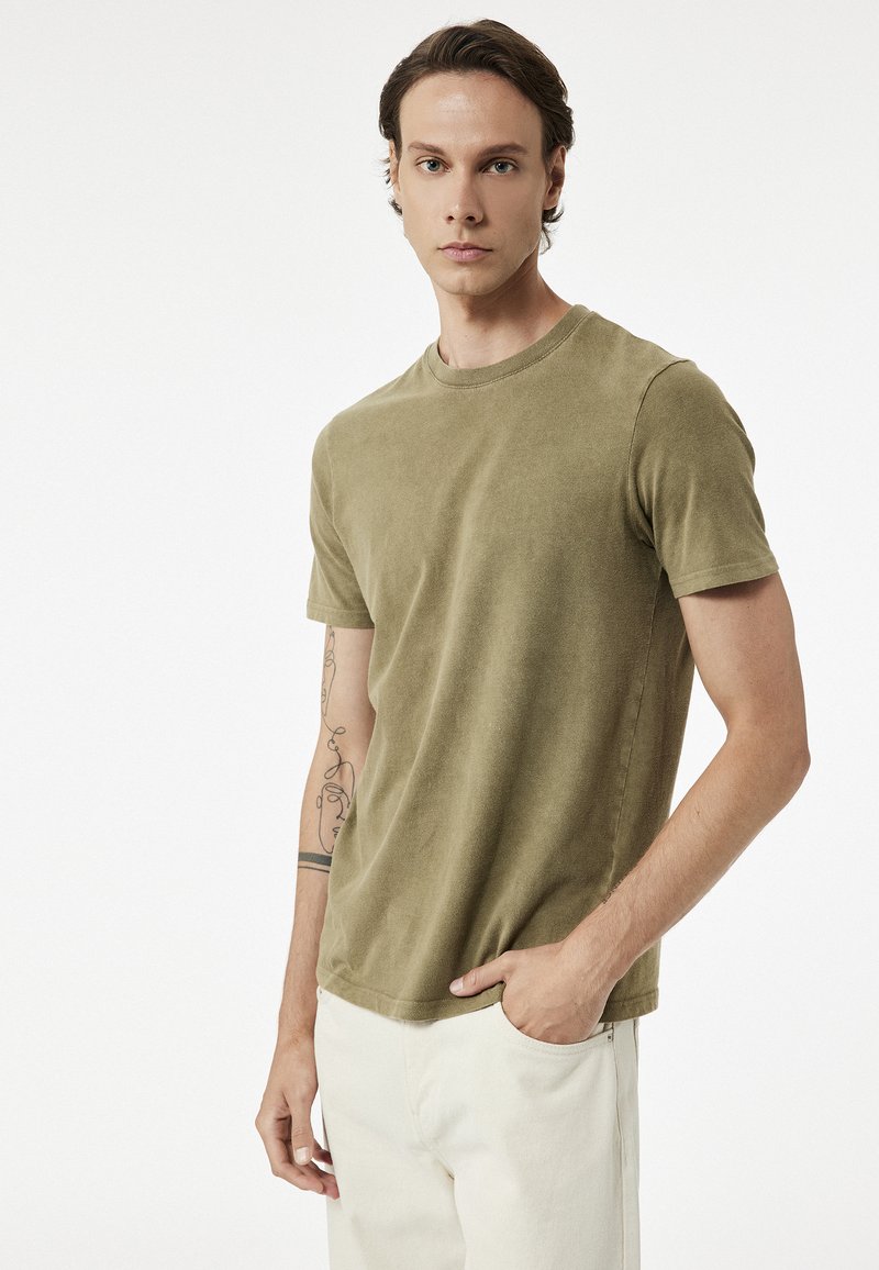 Oliwkowa bawełniana koszulka z klasycznym okrągłym dekoltem, krótkimi rękawami i miękkim, teksturowanym wykończeniem. Posiada luźny krój.