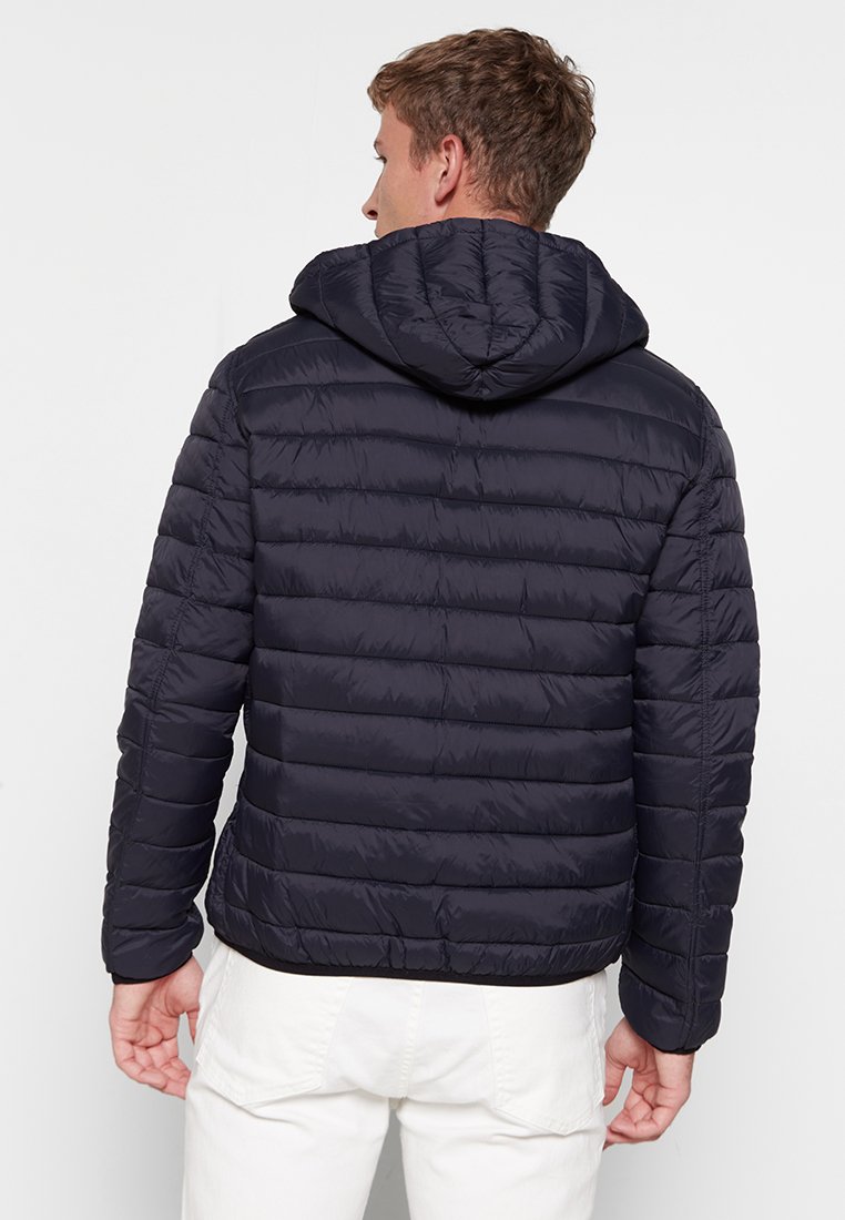 Marineblauwe pufferjack met horizontale quiltpatroon, een capuchon en elastische manchetten. Heeft een lichte textuur en een aansluitende snit.