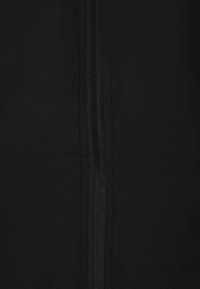 Sort stof med en glat tekstur, som har en central lynlåsdetalje. Designet er minimalistisk og fremhæver en ensartet farve uden mønstre.