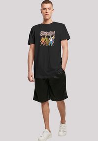 Svart bomull t-skjorte med "Scooby-Doo!" grafikk. Designet inkluderer fargerike tegneseriefigurer på fronten, som kompletterer avslappede shorts.