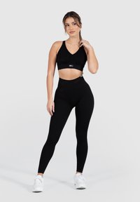 Top corto sportivo nero con scollatura a V e texture a costine, abbinato a leggings neri a vita alta, completato da sneakers bianche.