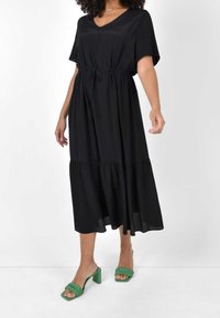 Svart midi-klänning med V-ringning, korta ärmar, dragsko i midjan och lagerkjol. Matchad med gröna klacksandaler med flätade remmar.