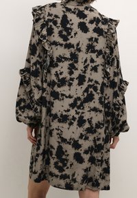 Vestido de manga larga con volantes en una tela beige con un patrón de manchas negras. Presenta un cuello mandarin y un corte holgado.