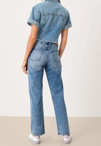 Denimová zkrácená košile s krátkým rukávem, světle modré barvy a nerovným lemem. Spárovaná s vysokými světle modrými džíny a bílými teniskami.